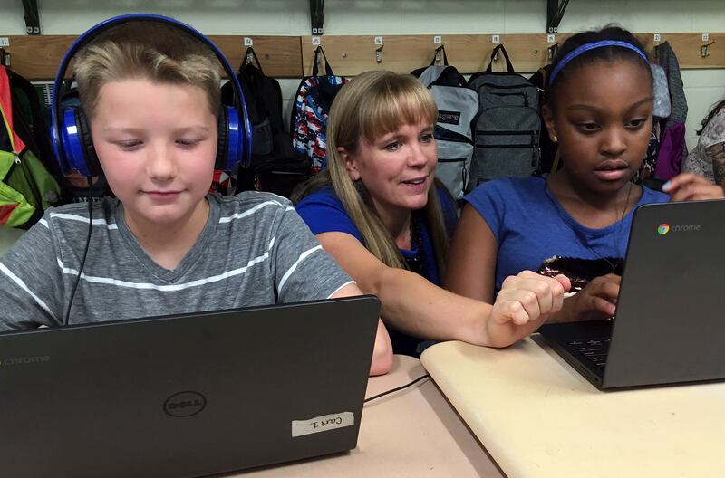 In this Sept. 20, 2018 photo, fifth grade teacher Heather Dalton, center, works with students Julian Ryno, left, and Ma'Kenley Burns, doing math problems on the DreamBox system at Charles Barnum Elementary School in Groton, Conn. (AP Photo/Michael Melia)