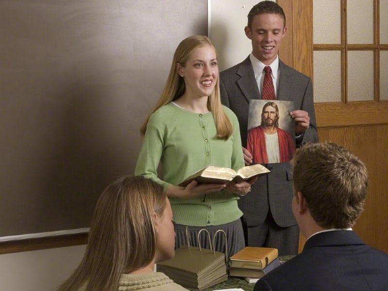 A woman stands at the front of a Sunday School class, teaching from the scriptures.