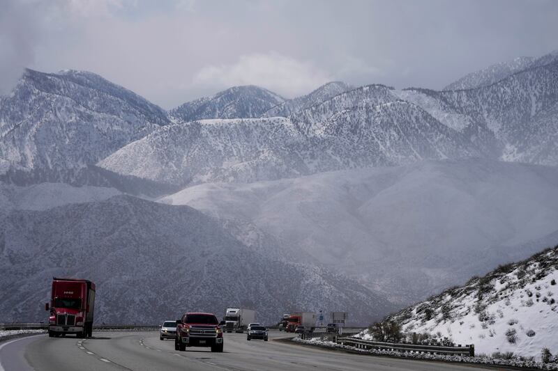 Vehicles make their way along the I-15 as clouds pass through the snow-covered mountains near Hesperia, Calif.