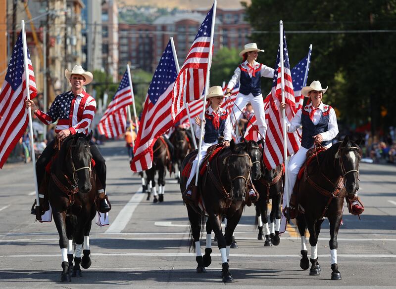People dressed in American Flag attire holding American Flags ride horses in a parade.
