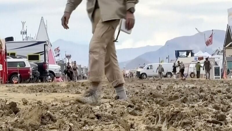 In this image from video provided by Stringr, a man walks through mud at the Burning Man festival site in Black Rock, Nev.