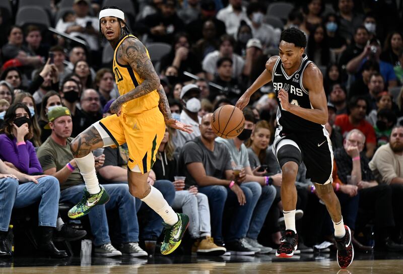 Utah Jazz’s Jordan Clarkson, wearing yellow, passes behind his back as he is defended by San Antonio Spurs’ Devin Vassell
