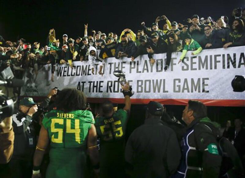 Oregon lineman Hroniss Grasu (55) hoists the trophy towards fans followed by offensive lineman Hamani Stevens (54) after defeating Florida State in the Rose Bowl NCAA college football playoff semifinal, Thursday, Jan. 1, 2015, in Pasadena, Calif.