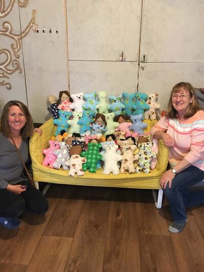 Merri-Lu Jackman, left, and Jennie White, right, pose with dolls and bears made by Yazidi survivors who live in a refugee camp in Serres, Greece. Dolls of Hope has established sewing centers in two refugee camps in Greece.