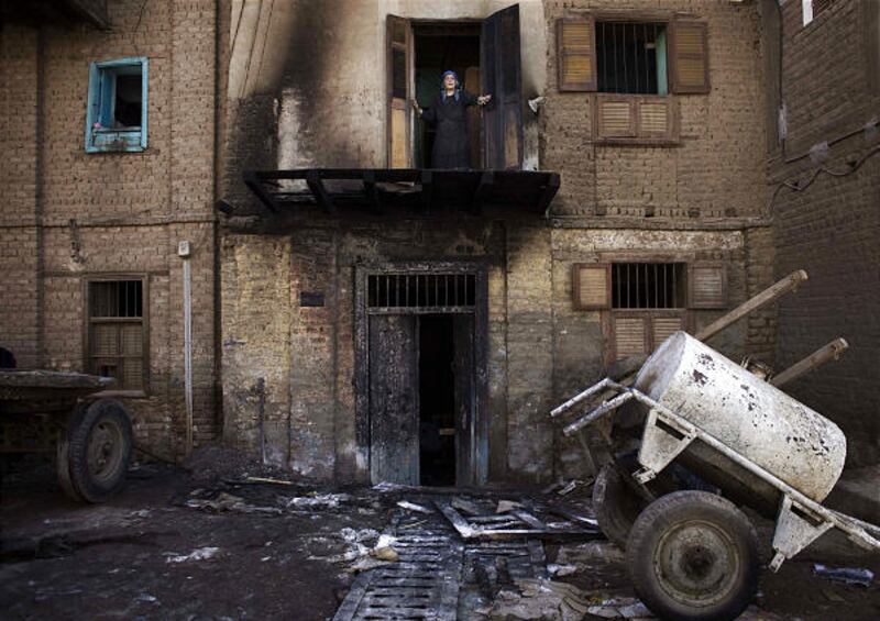An Egyptian woman looks out of her balcony Saturday from her partially burned house in Bahjora after an overnight arson attack that charred the homes of Coptic Christians.