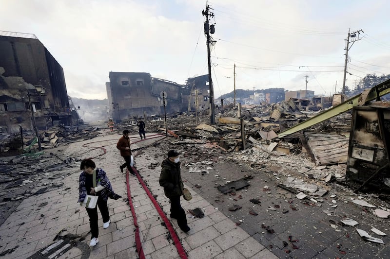 People walk past collapsed buildings following an earthquake in Wajima, Ishikawa prefecture, Japan, on Jan. 2, 2024.