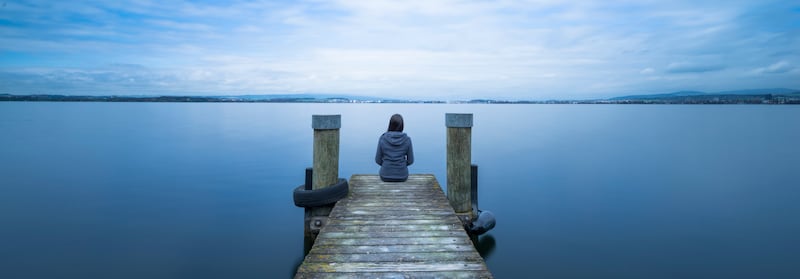 A woman sitting at the end of a pier on a lake.