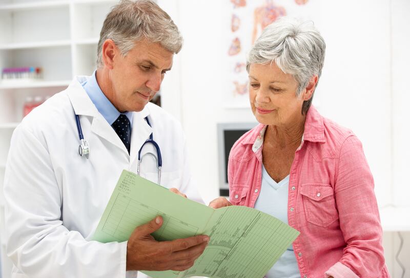 A doctor and a patient stand together looking over an open medical file.