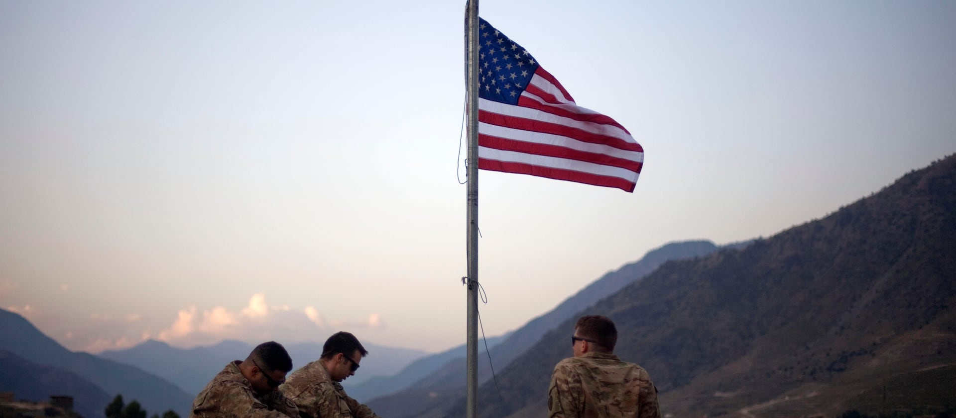 In this Sept. 11, 2011 file photo, US soldiers sit beneath an American flag just raised to commemorate the tenth anniversary of the 9/11 attacks at Forward Operating Base Bostick in Kunar province, Afghanistan.