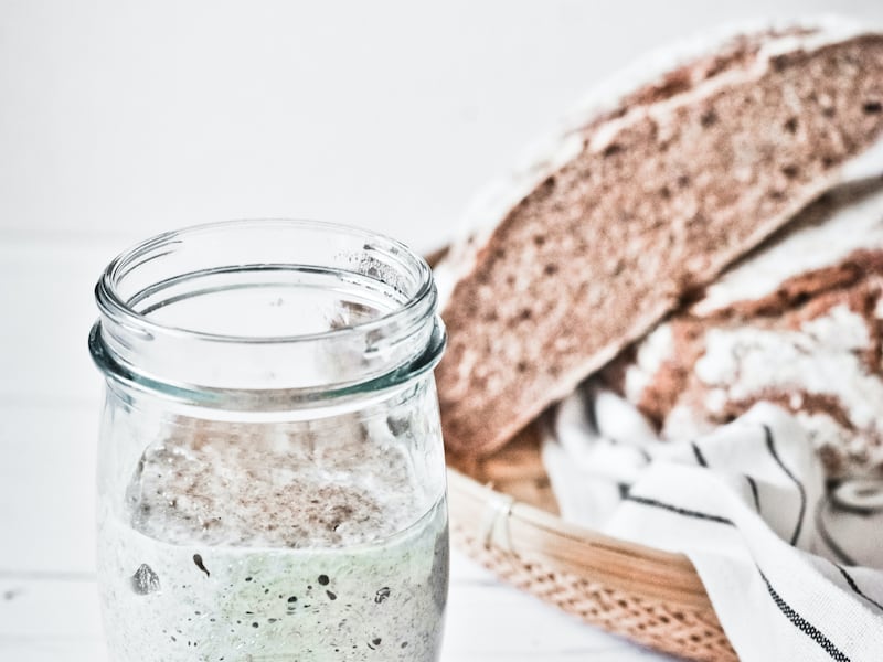 Sourdough starter in a jar with bread behind it.