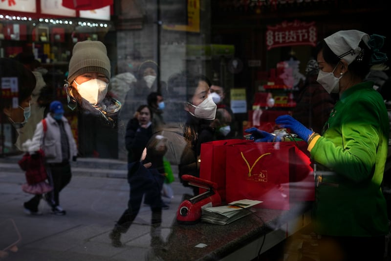 People are reflected on a window panel as visitors wearing face masks buy tea products in Beijing.