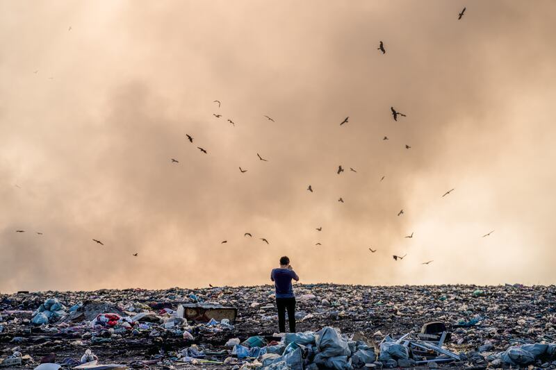 Person standing on a landfill full of garbage and burning garbage piles