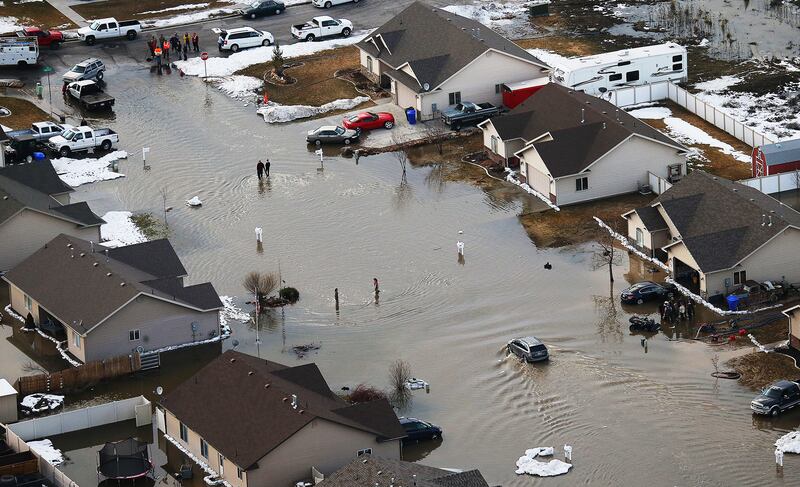 Residents walk and drive in water on a flooded street in Tremonton on Feb. 19, 2017.