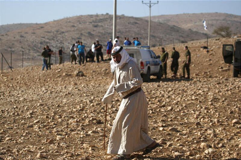 With Israeli soldiers and Jewish settlers in the background, a Bedouin man leaves an area which was fenced off by Jewish settlers in the West Bank village of Khirbet Ein al-Hilweh, in the Jordan Valley, Tuesday.