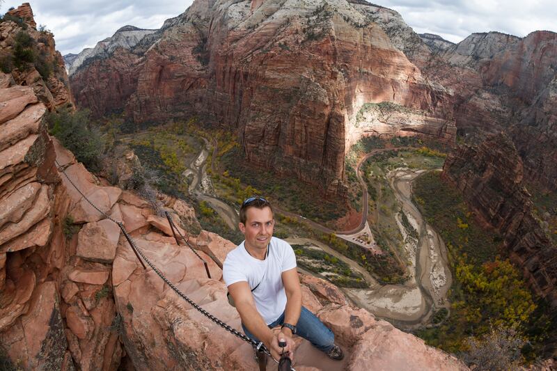 A man takes a selfie over the steep cliffs of the Angel's Landing hiking trail in Zion National Park.