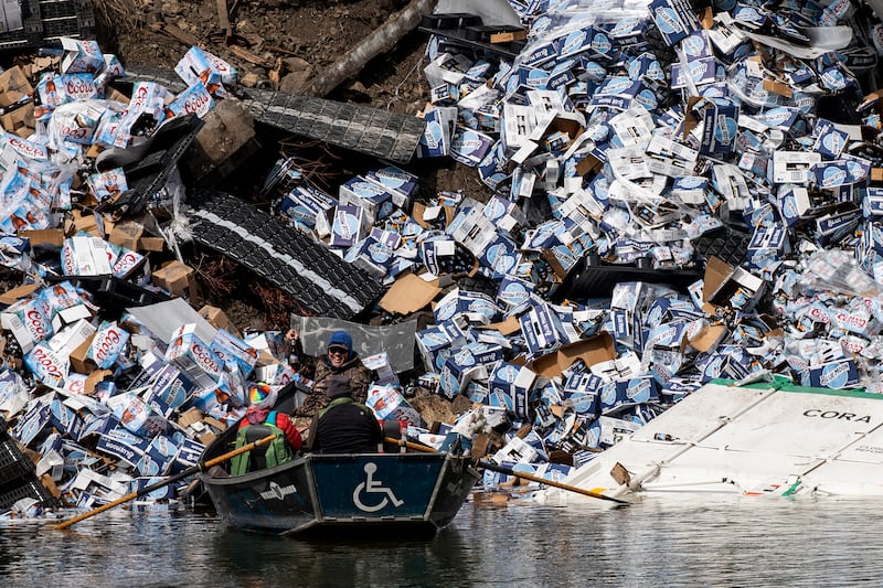 A group of fishermen claim a bottle of beer from a derailed railcar on the banks of the Clark Fork River near Quinn’s Hot Springs, west of St. Regis, Mont., Sunday, April 2, 2023. Montana Rail Link is investigating the derailment in which there were no injuries reported.