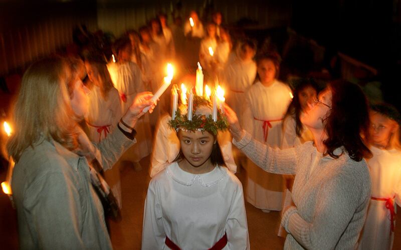 Eleven-year-old Julia Phan, with parents of Vietnamese origin, stands still as Rose-Marie von Braun, left, and Anne-Marie Soderqvist, right, light candles in Julia’s crown of Lucia “Queen of lights.”
