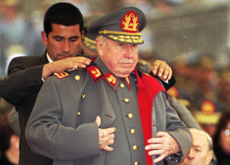 FILE - In this Aug. 23, 1995 file photo, former Chilean dictator and military commander Gen. Augusto Pinochet is helped by a bodyguard to put on his coat during a military ceremony in Santiago, Chile, on the occasion of the 22nd anniversary of his taking