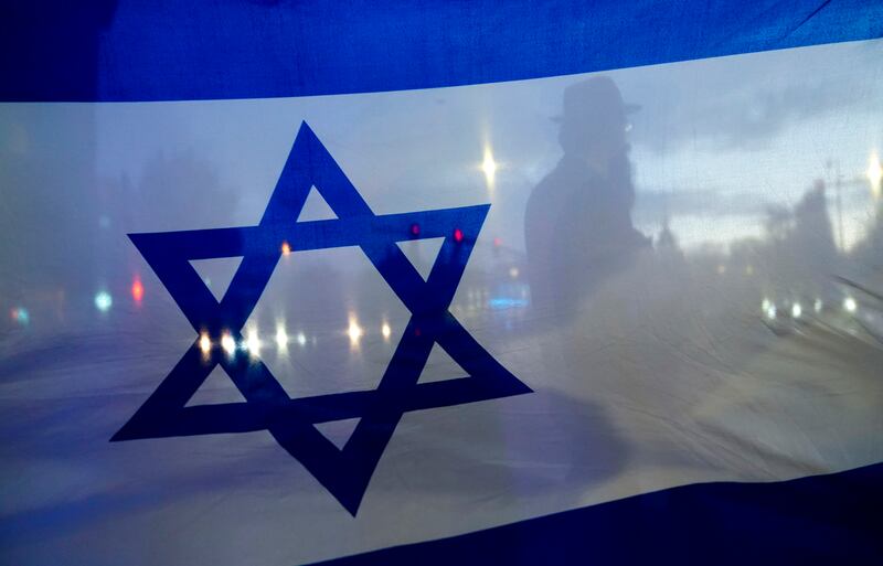 A demonstrator crossing the street is silhouetted behind a flag of Israel during a rally in support of Israel Monday, Oct. 9, 2023, in Bellevue, Wash.