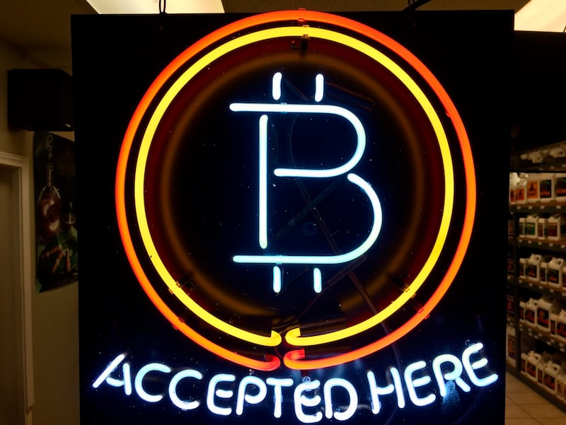 In this Feb. 7, 2018 file photo, a neon sign hanging in the window of Healthy Harvest Indoor Gardening in Hillsboro, Ore., shows that the business accepts bitcoin as payment.