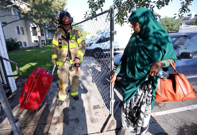 Salt Lake City firefighter Kade Martin recovers a suitcase from an apartment for Hodan Hirsi after a fire at the Seasons at Pebble Creek Apartments on Wednesday, Aug. 8, 2018.