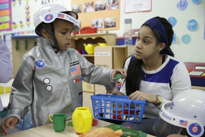 In this Tuesday, Jan. 21, 2014 photo, Bryson Payne, 4, left, and his teacher Jacqualine Sanchez play with pretend food in a pre-kindergarten class at the Sheltering Arms Learning Center in New York. New studies show kids learn advanced material much earli