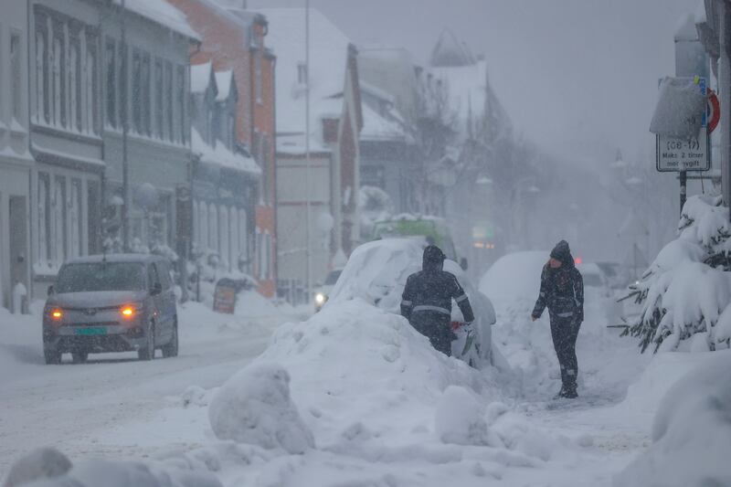 People attempt to clear the snow off a vehicle in Kristiansand, Norway, on Tuesday, Jan. 2, 2024.