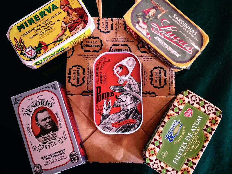 A variety of flavored, gourmet canned sardines are shown in colorful, decorative tins.