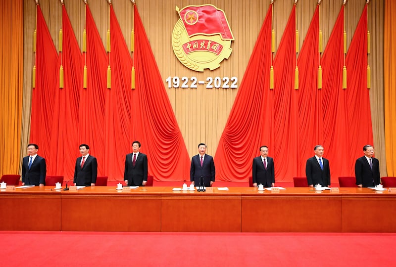 Chinese President Xi Jinping stands with six other Chinese leaders against a wall draped with striking red fabric.