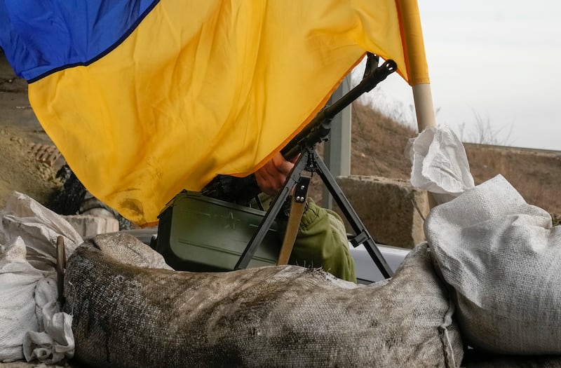 A machine gun emerges from under the Ukrainian flag on a front-line position near Kharkiv, Ukraine, on Saturday, March 26, 2022.