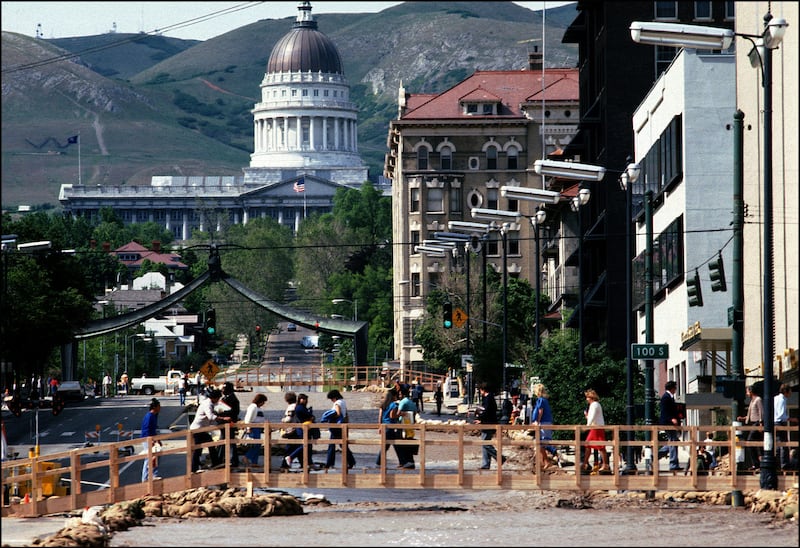 People cross a makeshift bridge over a flooded State Street in Salt Lake City in 1983. The river was the result of massive debris buildup that blocked four blocks worth of pipes beginning by the mouth of City Creek Canyon.