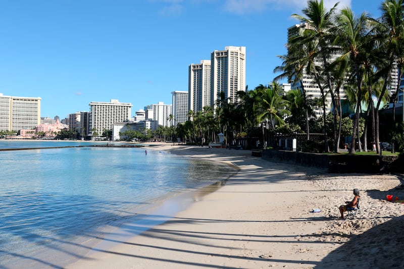 A man sits on a nearly empty Waikiki Beach in Honolulu, Friday, Oct. 2, 2020. After a summer marked by a surge of coronavirus cases in Hawaii, officials plan to reboot the tourism based economy later this month despite concerns about the state’s pre-travel testing program.