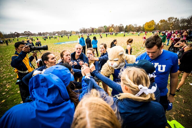 The BYU women's cross-country team, joined by Cosmo (right), prepares for a meet with a team chant.