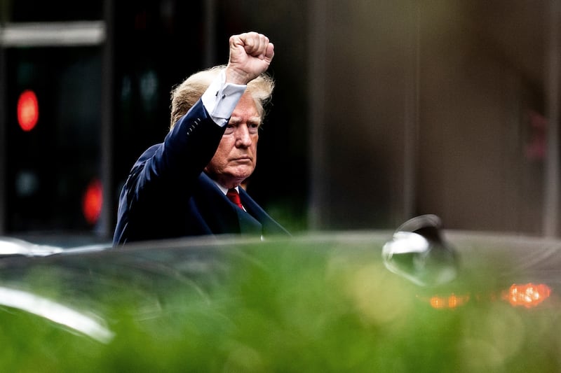 Donald Trump holds a fist in the air with a stern face before getting into a car.
