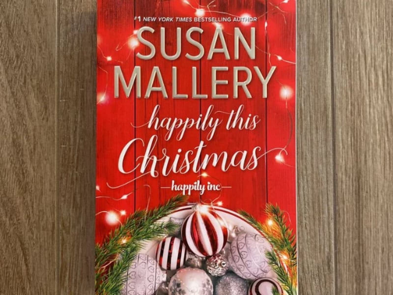 The book “Happily This Christmas” by Susan Mallery sits on a table.