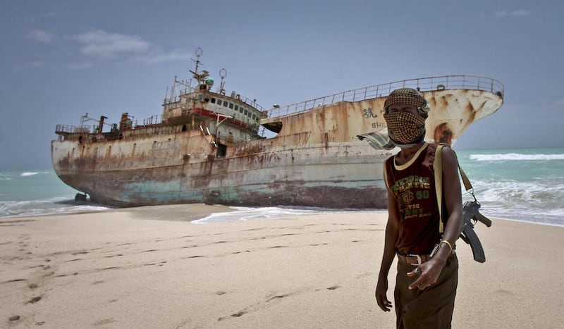 In this photo taken Sunday, Sept. 23, 2012, masked Somali pirate Abdi Ali stands near a Taiwanese fishing vessel that washed up on shore after the pirates were paid a ransom and released the crew, in the once-bustling pirate den of Hobyo, Somalia.