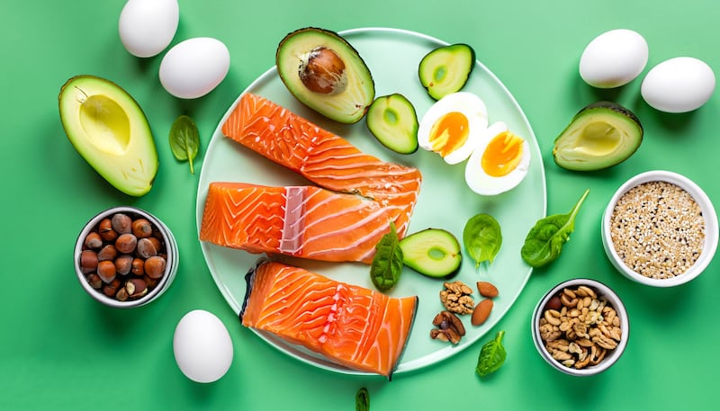 A plate of food including salmon, avocado, nuts and eggs.
