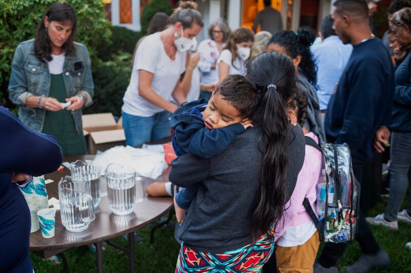 A woman, who is part of a group of immigrants that had just arrived, holds a child as they are fed outside St. Andrews Episcopal Church, Sept. 14, 2022, in Edgartown, Mass., on Martha’s Vineyard.
