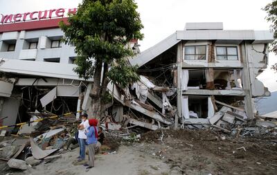 Filipinos stand beside the heavily damaged Mercure hotel after a massive earthquake and tsunami hit Palu, Central Sulawesi, Indonesia Thursday, Oct. 4, 2018. Life is on hold for thousands living in tents and shelters in the Indonesian city hit by a powerf