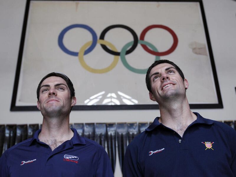 In this May 7, 2012, shows American Olympic rowers Ross James, left, and his twin brother, Grant James, right, pose next to an Olympic flag at the rowing office in Oakland, Calif. Both will be competing in the London Olympics.