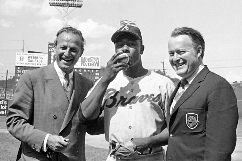 In this May 17, 1970, file photo, Atlanta Braves’ Hank Aaron, center, who became the ninth player in Major League history to get 3,000 hits, kisses a baseball alongside Famer Stan Musial and Braves owner Bill Bartholomay, in Cincinnati.
