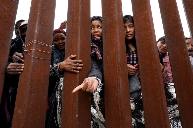 Migrants waiting to apply for asylum reach through a border wall for clothing handed out by volunteers on May 12, 2023, in San Diego.