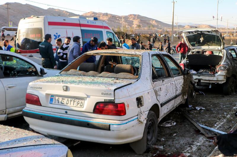 People stay next to destroyed cars after an explosion in Kerman, Iran, on Wednesday, Jan. 3, 2024.