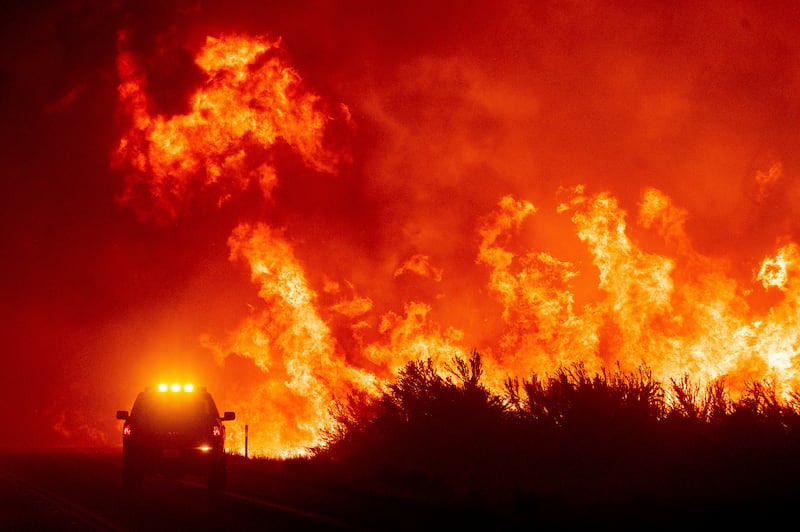 Flames leap above a fire vehicle as the Dixie Fire jumps Highway 395.