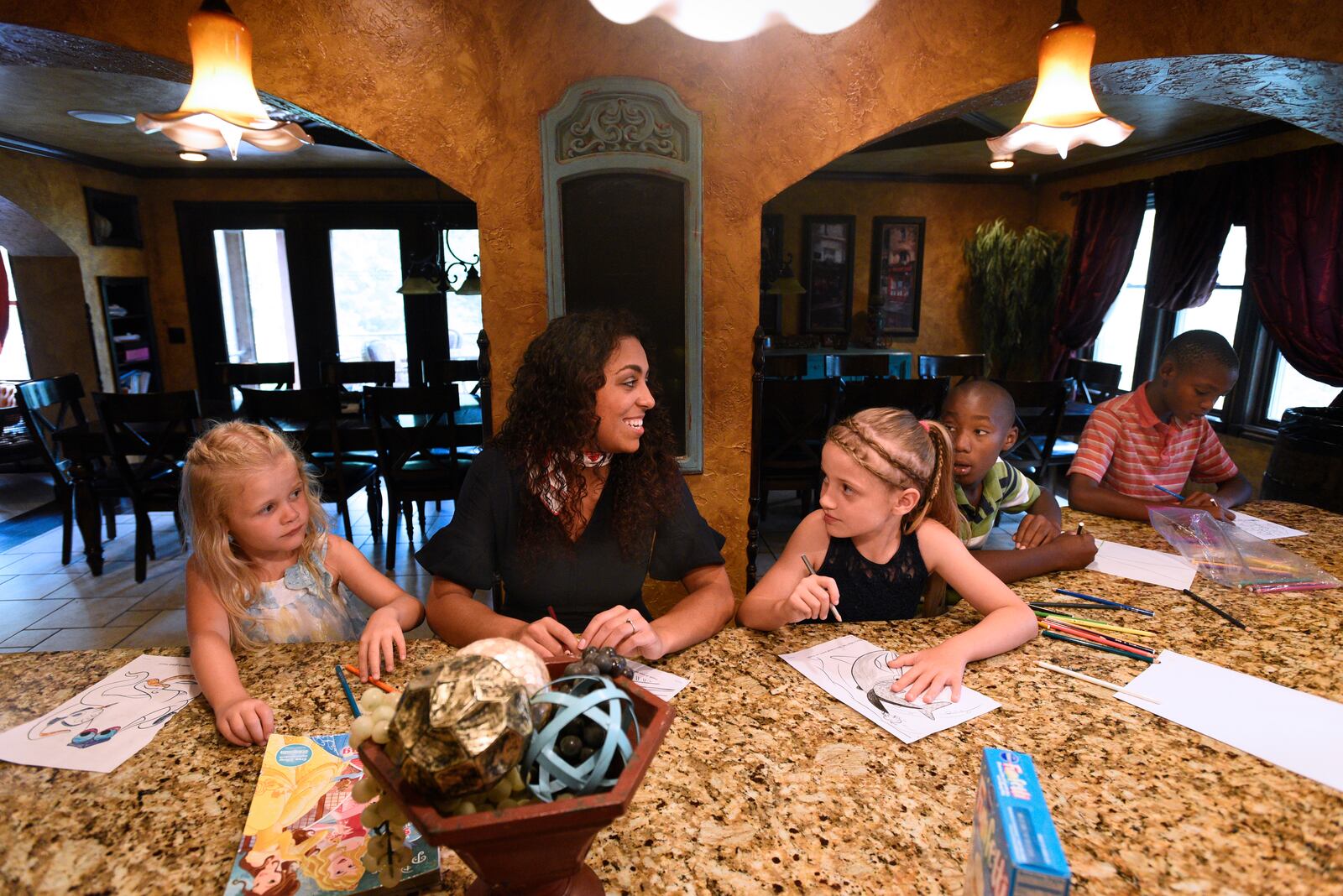 Shamber Flore, 20, center, talks and colors with younger siblings Jubilee, 7, Mercy, 9, Marcus, 10, and Lucas, 10, left to right, in the family's kitchen and dining room area at home in DeWitt, Michigan, on June 18, 2018. The Flore family has adopted thro