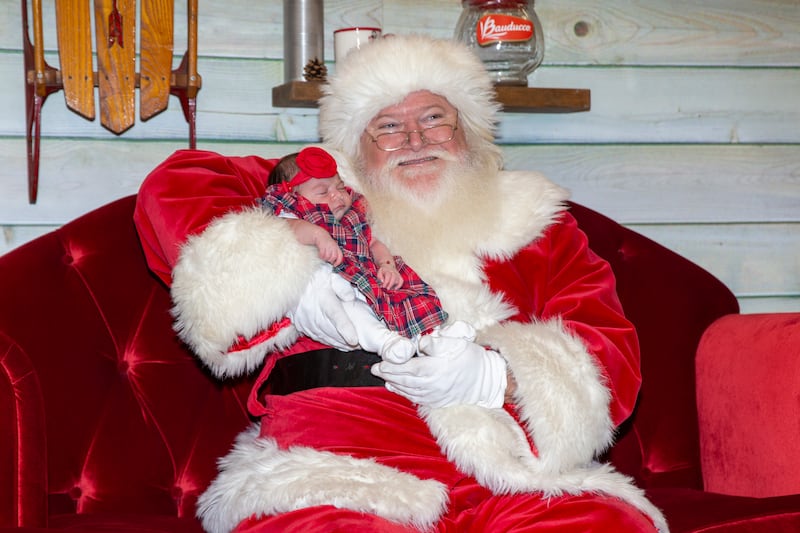 A man portraying Santa poses for photos with a 2-week-old baby.