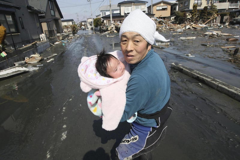 FILE - In this March 14, 2011 file photo, upon hearing another tsunami warning, Takatoshi Ishikawa tries to flee for safety with his recently-reunited four-month-old child Iroha, who was spotted by Japan's Self-Defense Force member in the rubble of tsunam