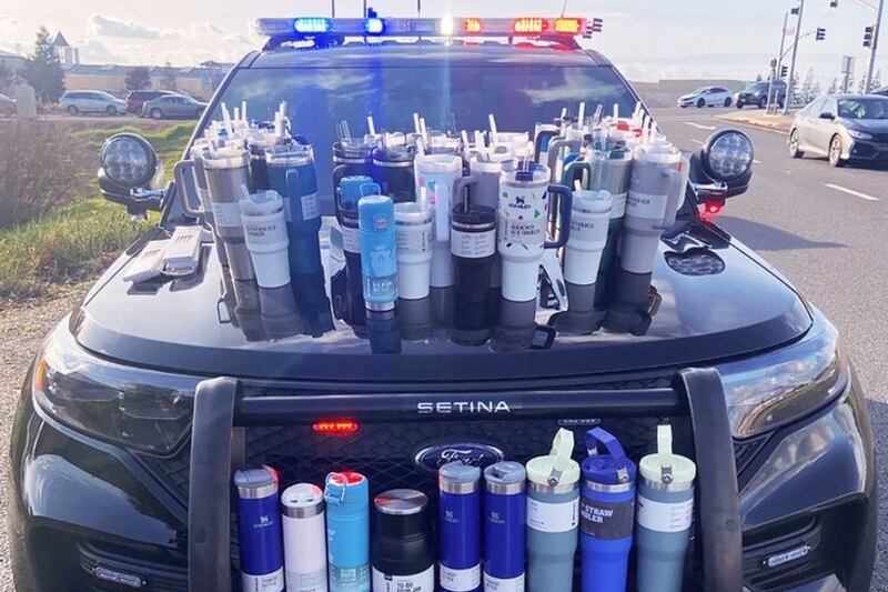Stanley cups are arranged on the hood of a police car. A 23-year-old Sacramento woman was arrested for theft after police searched her vehicle and found 65 Stanley stainless steel drinking products.
