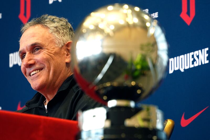 Duquesne University men's basketball coach Keith Dambrot sits next to the Atlantic 10 Championship trophy during a gathering in Pittsburgh celebrating Duquesne earning a berth in the NCAA Men's Basketball Tournament for the first time since 1977 Monday, March 18, 2024. Dambrot announced that he is retiring after his team's NCAA tournament run.