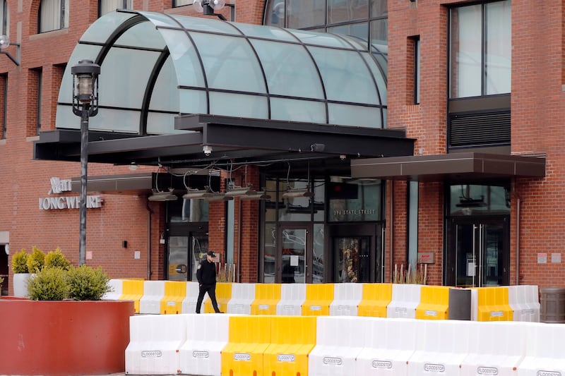 A security officer walks past the entrance of the closed Marriott Long Wharf hotel, Tuesday, April 21, 2020, in Boston. The new coronavirus was spread among Biogen executives who were meeting at the hotel in late February.